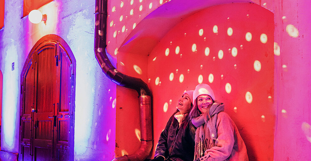 Two people sitting down at the Finlayson area which is illuminated with colourful light projections.